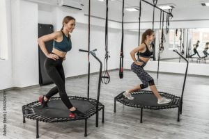 Portrait of two young pretty active girls and fitness trainer in sport clothes doing exercises for jump with trampoline during training in gym